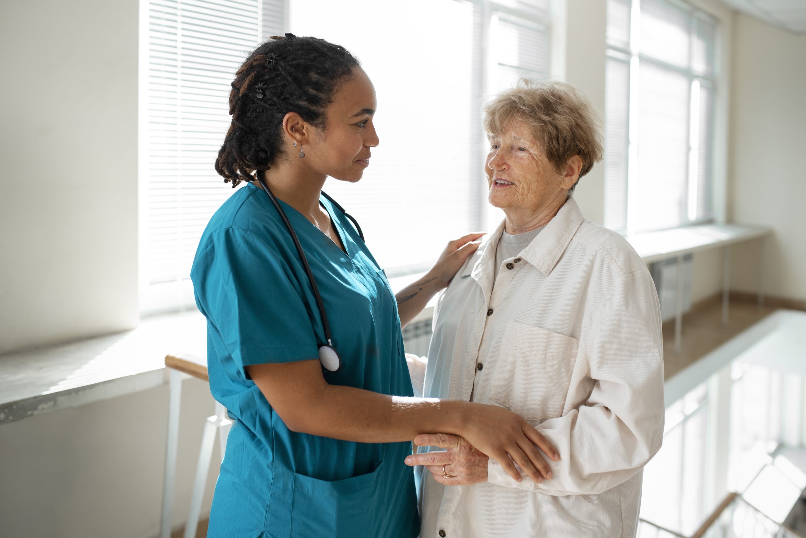 Enfermeira conversa com paciente idosa em um corredor