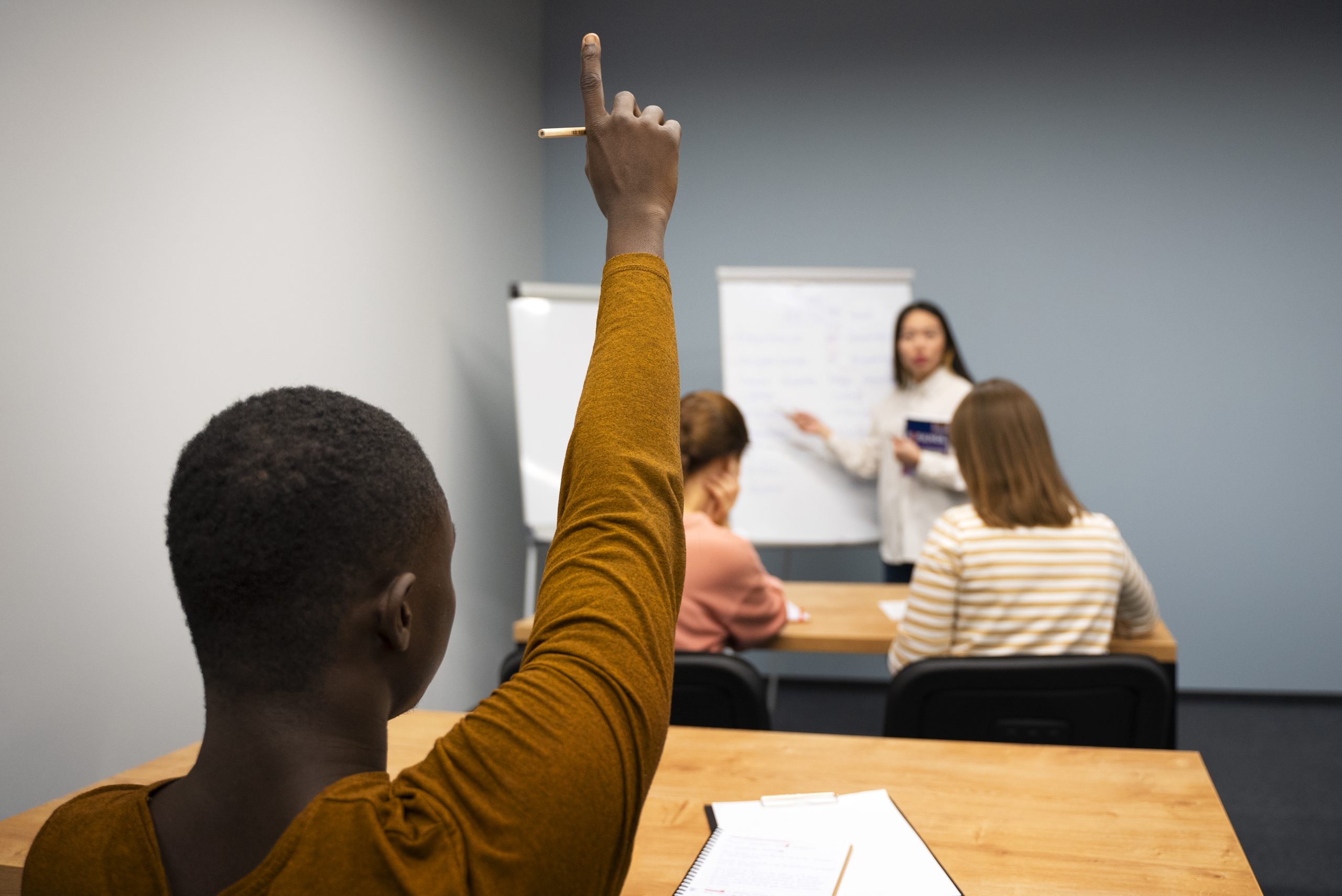 Professora interage com aluno que levanta a mão com dúvida