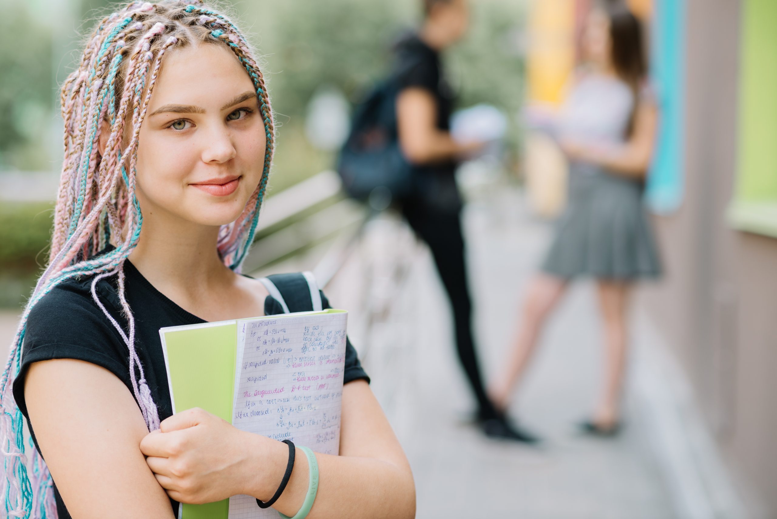 Adolescente segurando livro no campus da escola com colegas ao fundo